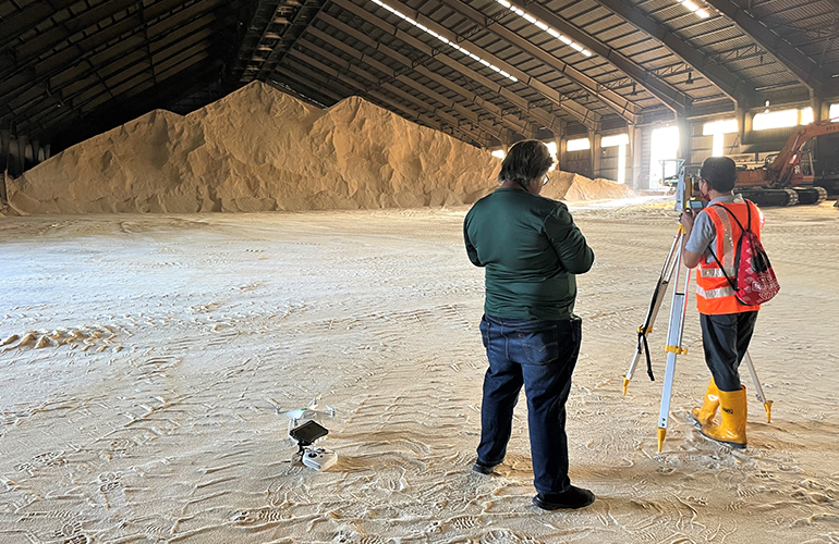 Surveyors standing near a large industrial stockpile for inventory management.