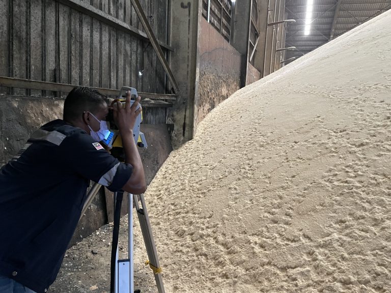 A surveyor using a total station for precise stockpile measurement in a warehouse.